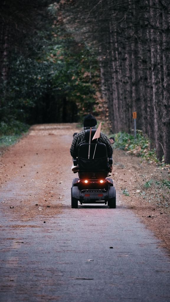 Elderly person riding a mobility scooter along a forest path, embracing nature.