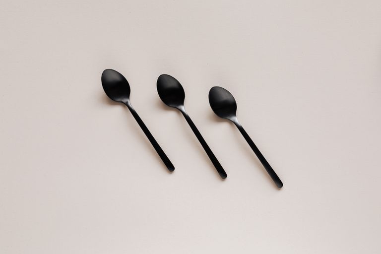 Top view composition of black stainless steel tea or dessert spoons of simple minimal design placed on gray kitchen counter or desk