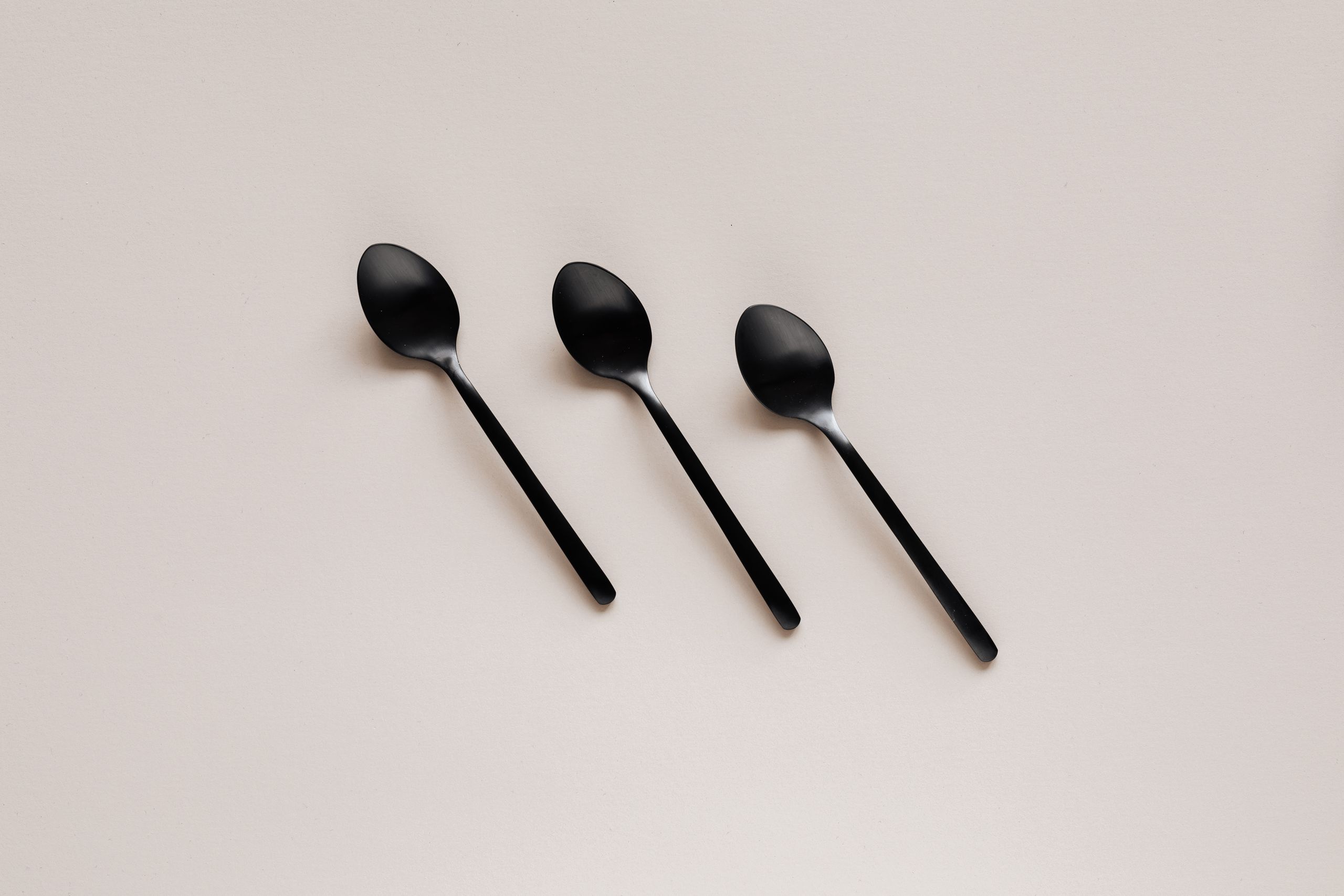 Top view composition of black stainless steel tea or dessert spoons of simple minimal design placed on gray kitchen counter or desk
