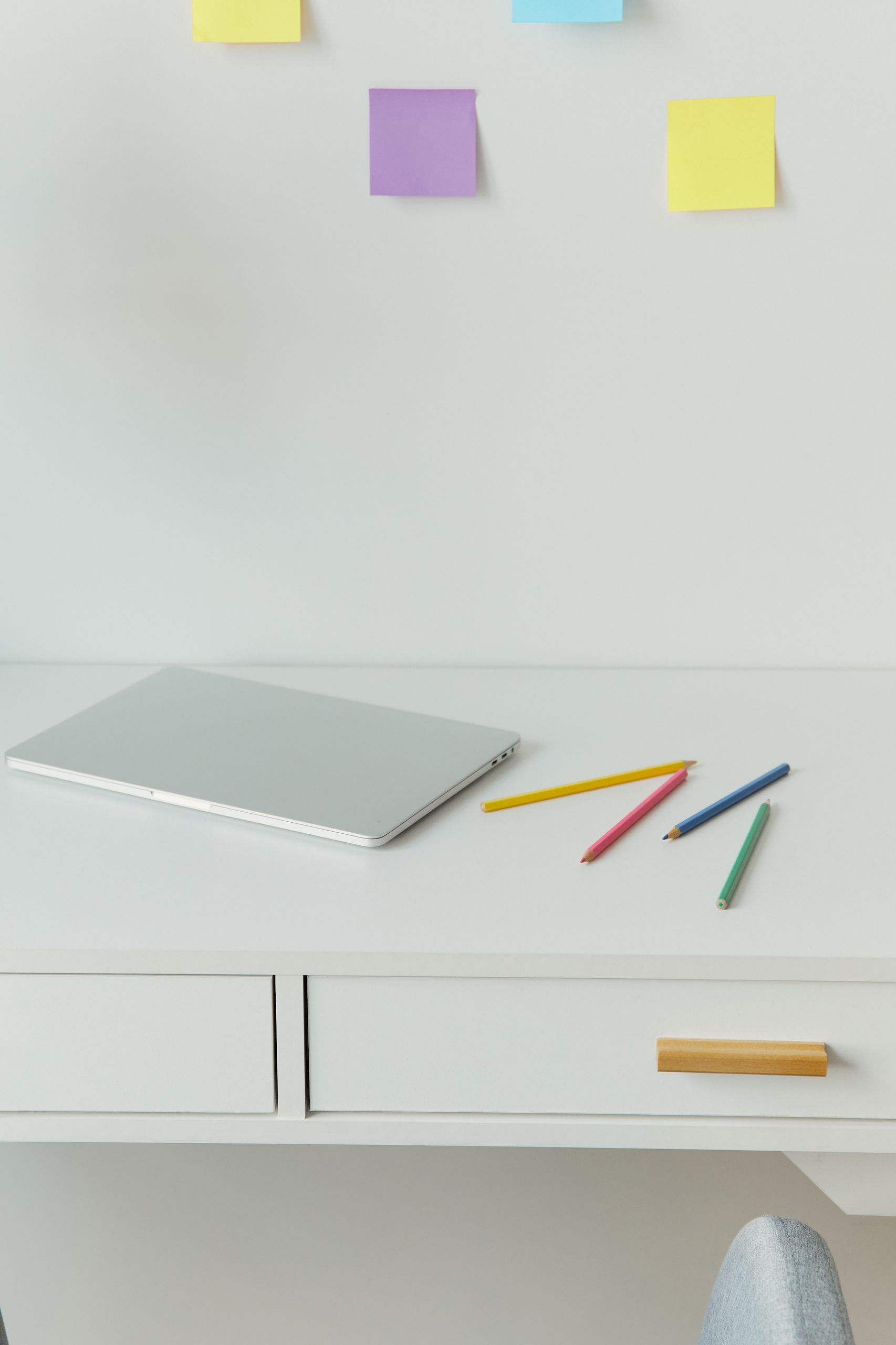 A minimalist home office desk with a laptop and colored pencils on a white surface.
