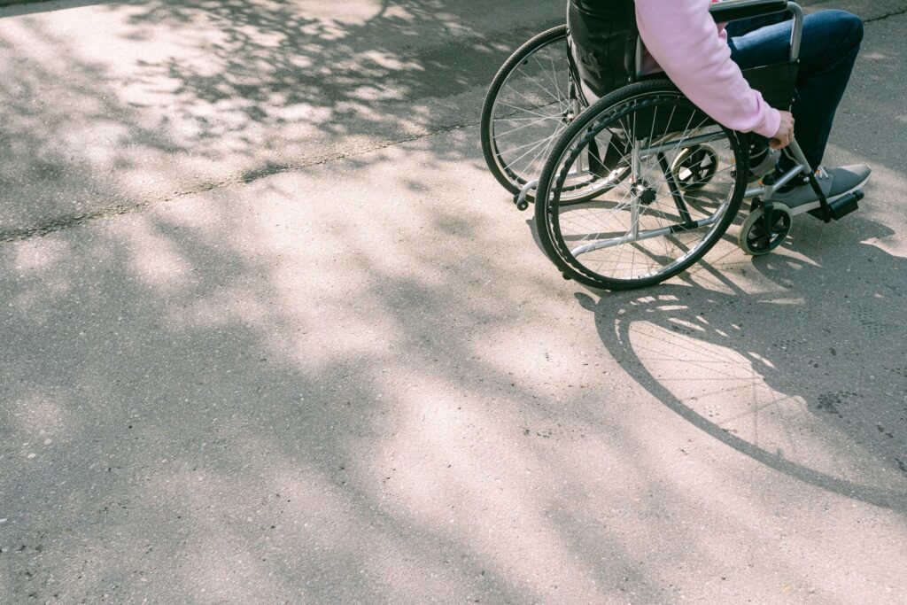 A person in a wheelchair navigating a sunlit road with tree shadows. The image captures a moment of mobility and independence.