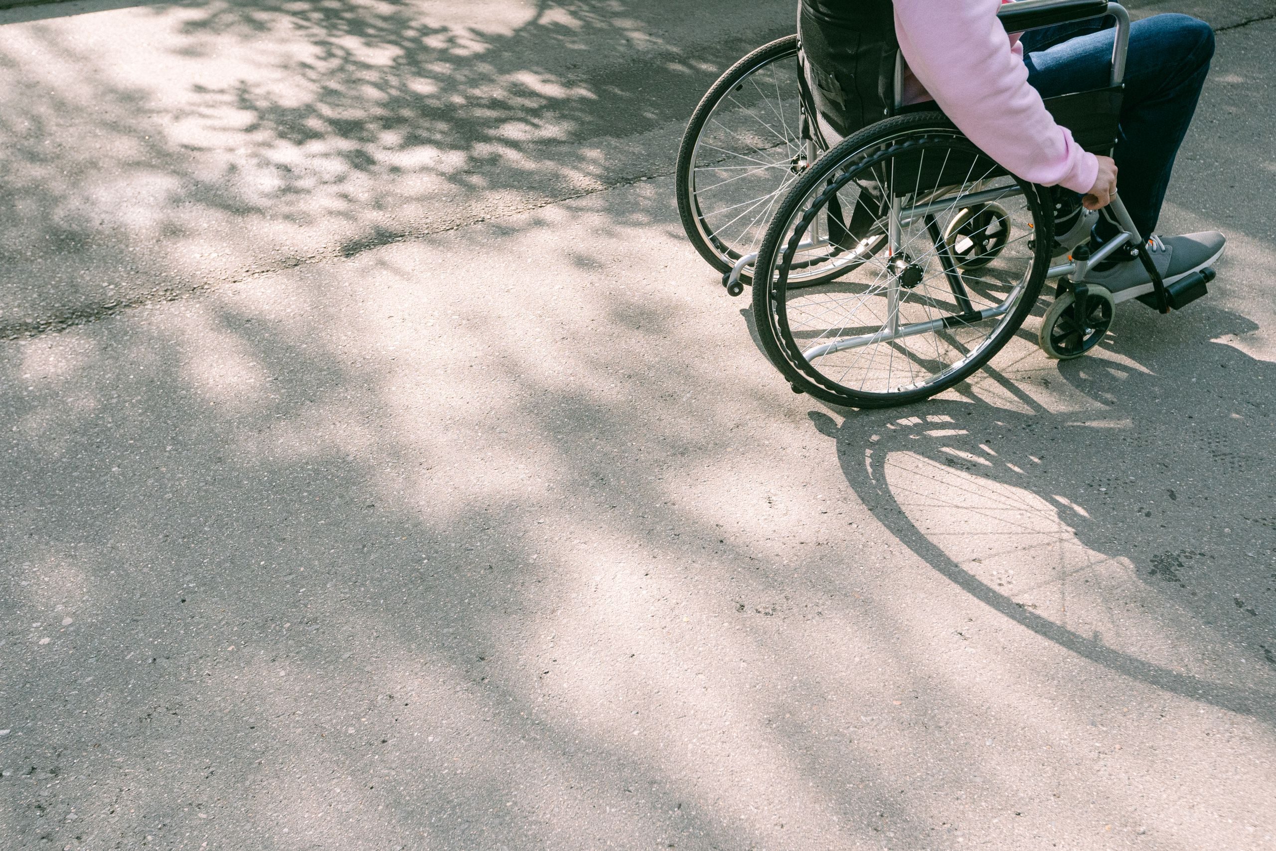 A person in a wheelchair navigating a sunlit road with tree shadows. The image captures a moment of mobility and independence.