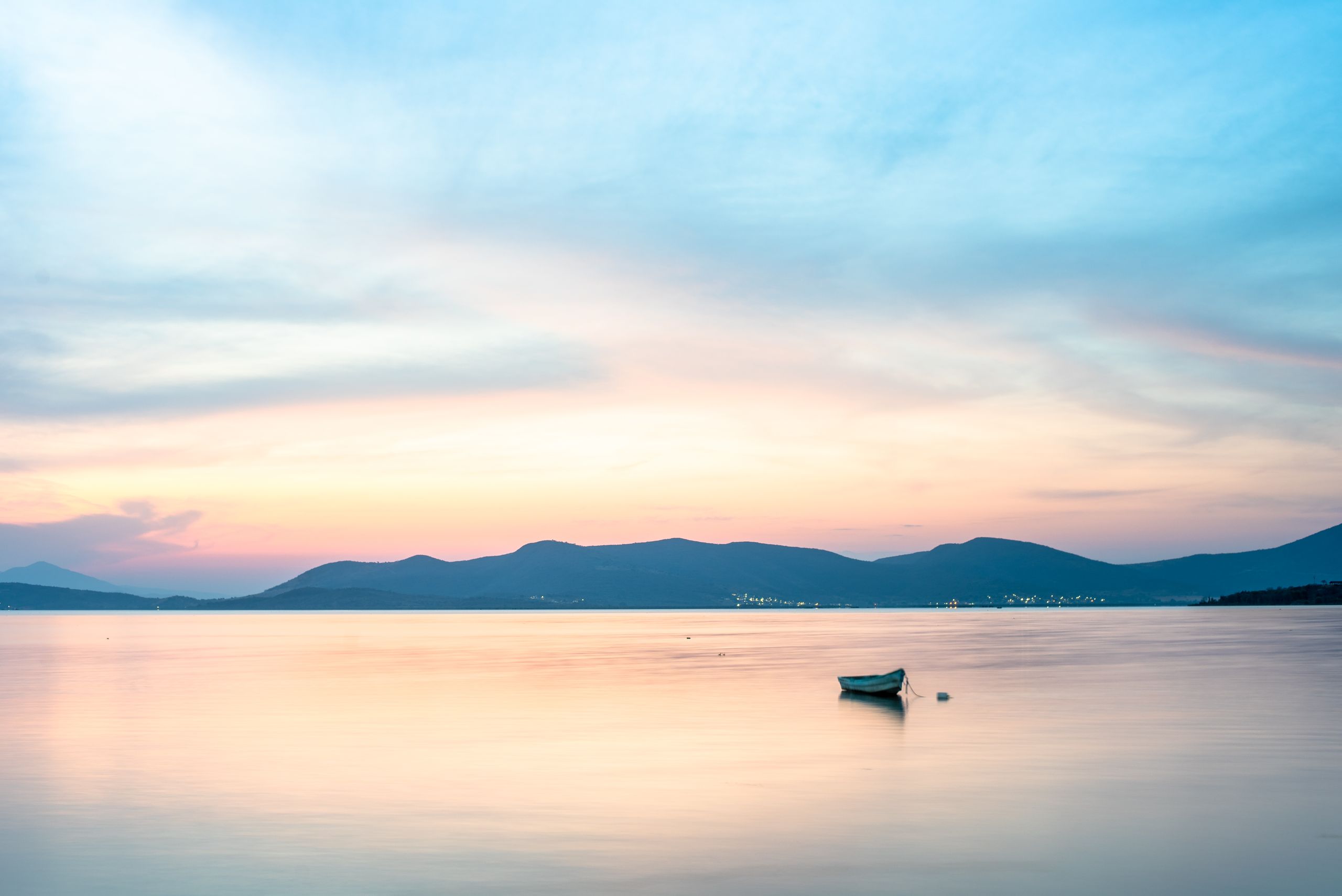 A tranquil evening scene featuring a lone boat on calm water with a stunning sunset and mountain silhouette.